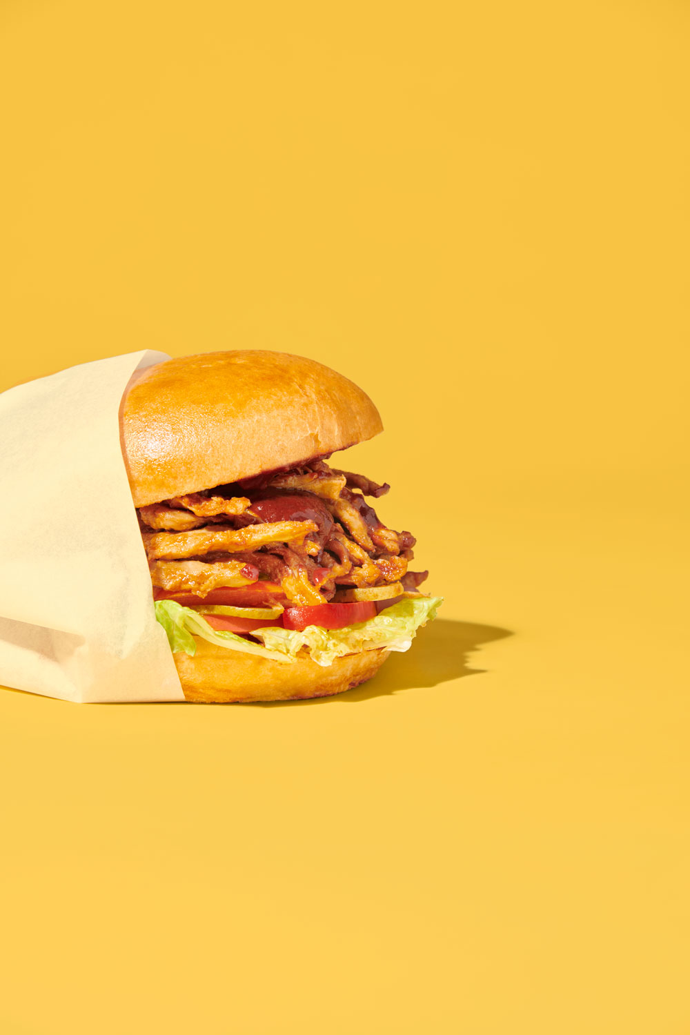 A planted.pulled burger wrapped in paper on a yellow background